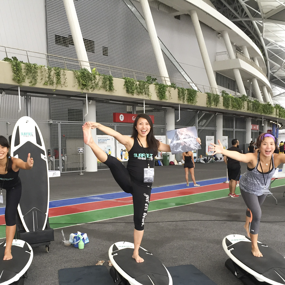 Instructors in yoga poses on surfset board during sweatfornepal